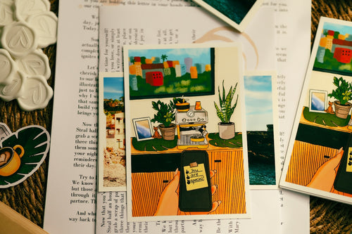 Hand holding a cozy illustrated postcard featuring a yellow espresso coffee maker, green house plants, and a bright city view.